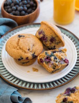 Healthy blueberry muffins on a white and blue plate with orange juice in the background.