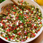 Lentil salad shown in a white ceramic serving bowl. Made with green lentils, bell pepper, red onion, feta, cucumber and dressing.