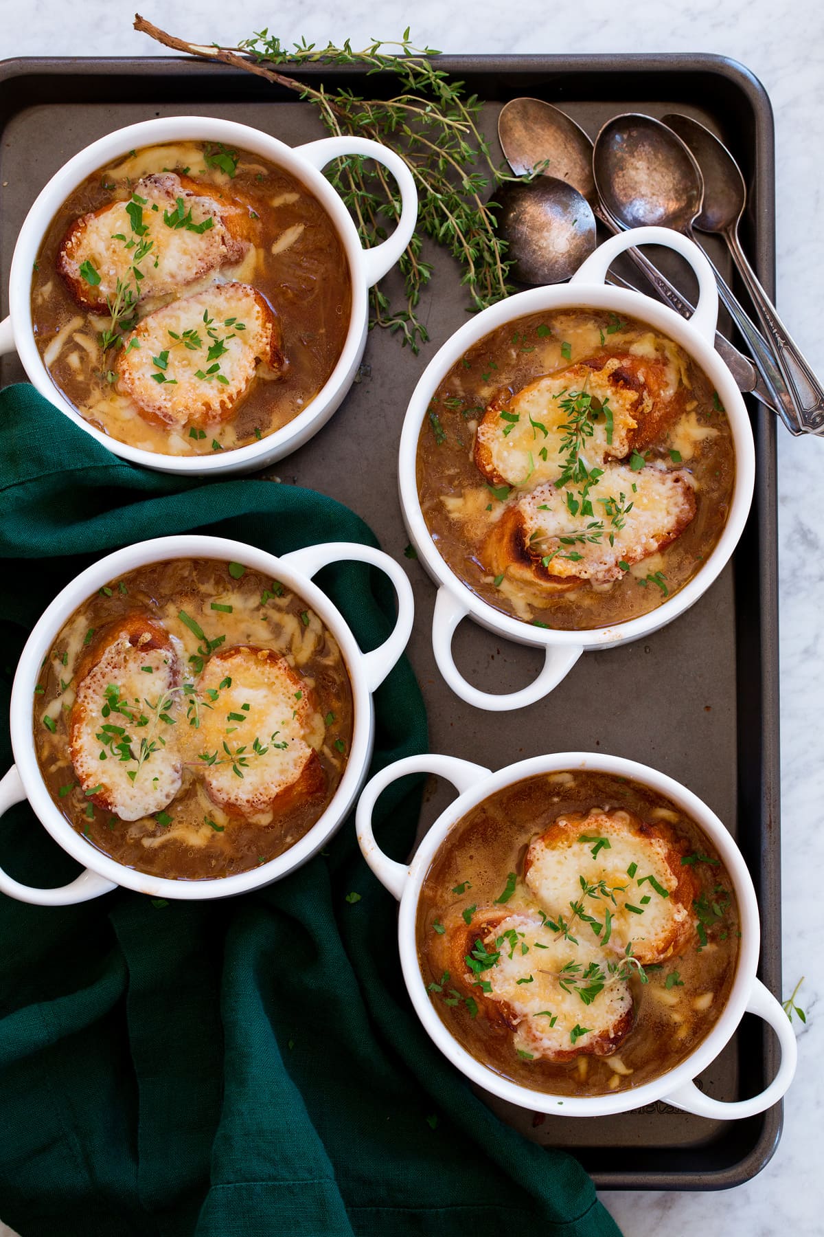 Four servings of french onion soup in white bowls with handles, shown from overhead on a dark baking sheet.