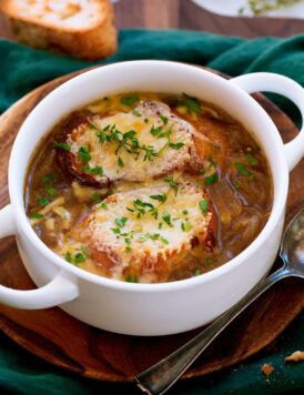 French onion soup shown in a white bowl with handles. Soup is topped with baguette slices, broiled cheese and herbs.