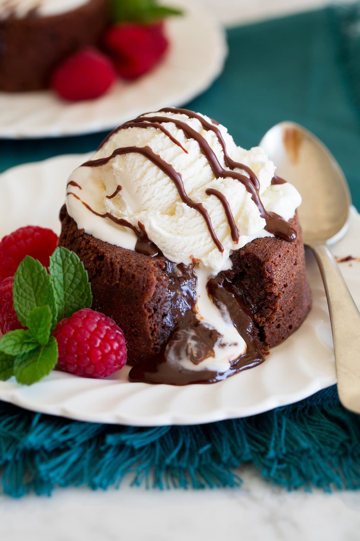 Chocolate lava cake on a serving plate with ice cream on top. Raspberries are shown to the side.