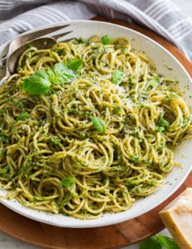 Homemade pesto tossed with spaghetti pasta in a large white serving bowl set over a wooden platter.