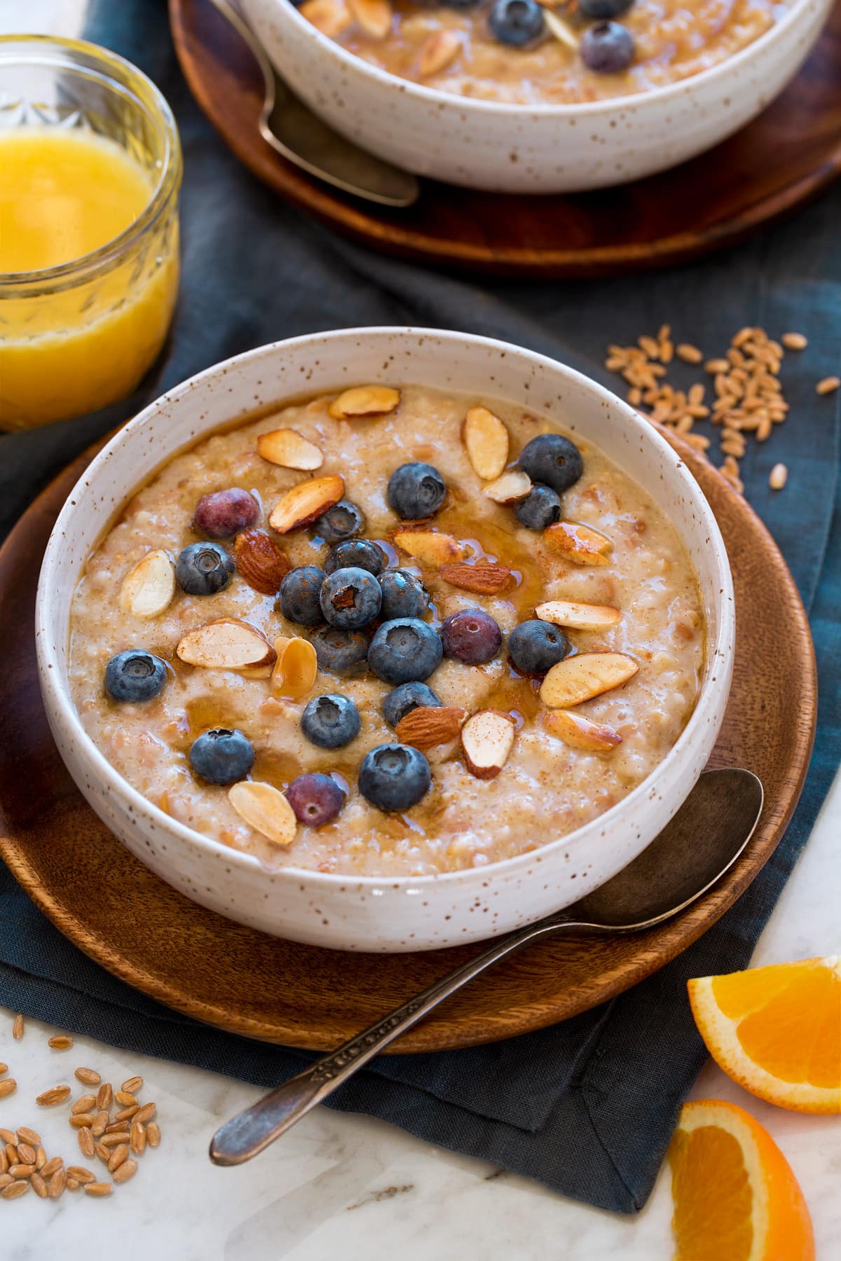 Multigrain porridge made with steel cut oats, farro and amaranth. It is shown served with fresh blueberries, sliced almond and maple syrup.