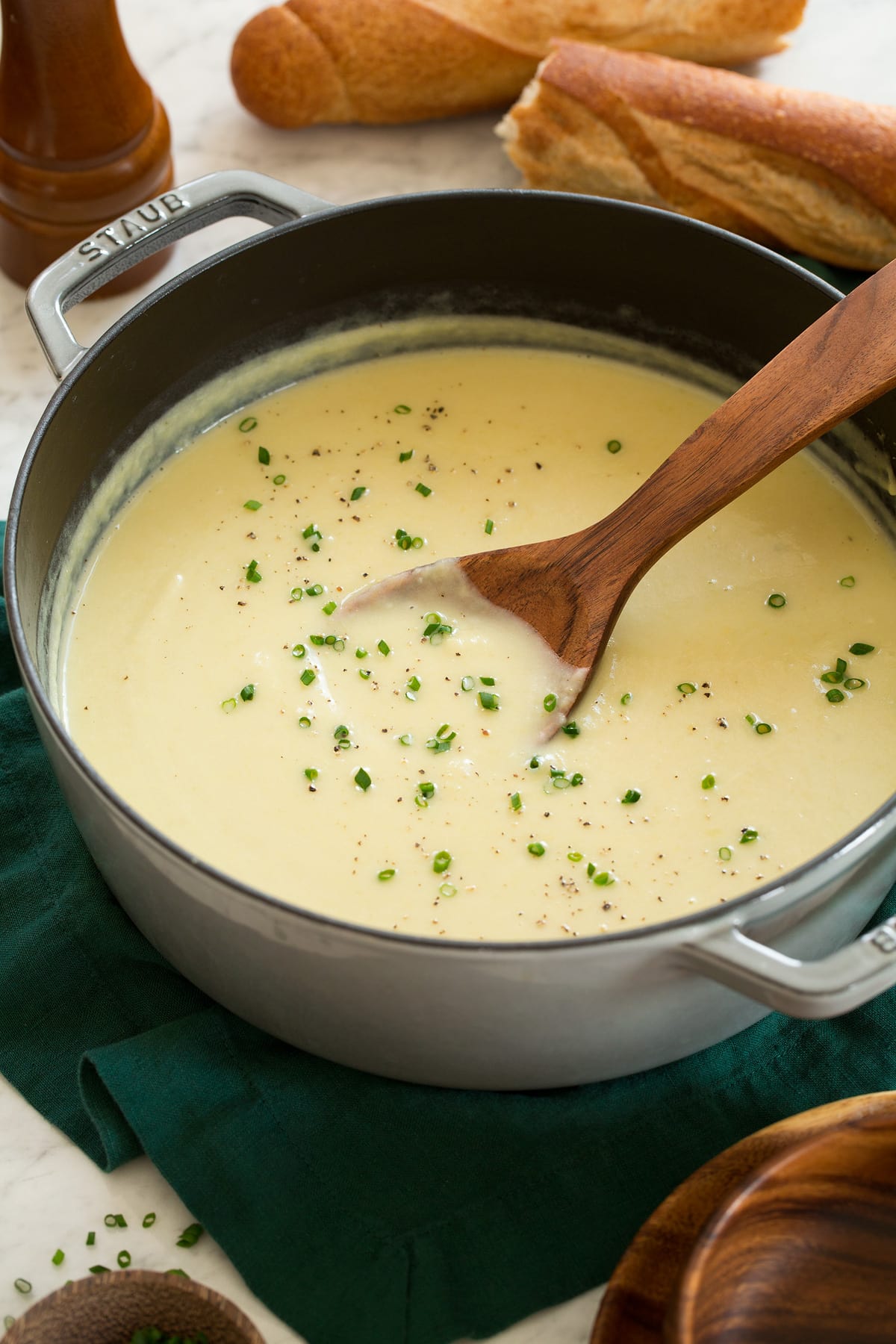 Pot with potato leek soup garnished with chives and a wooden ladle is scooping soup.
