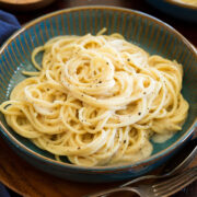 Cacio e pepe in a blue serving bowl over a wooden plate and table.