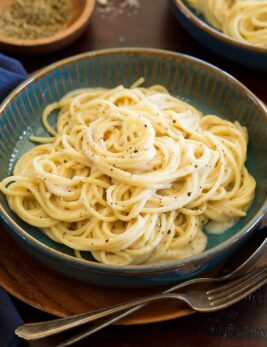 Cacio e pepe in a blue serving bowl over a wooden plate and table.