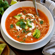 Sopa de fideo in a white soup bowl. Shown topped with avocado, cilantro, mexican crema, and queso fresco.