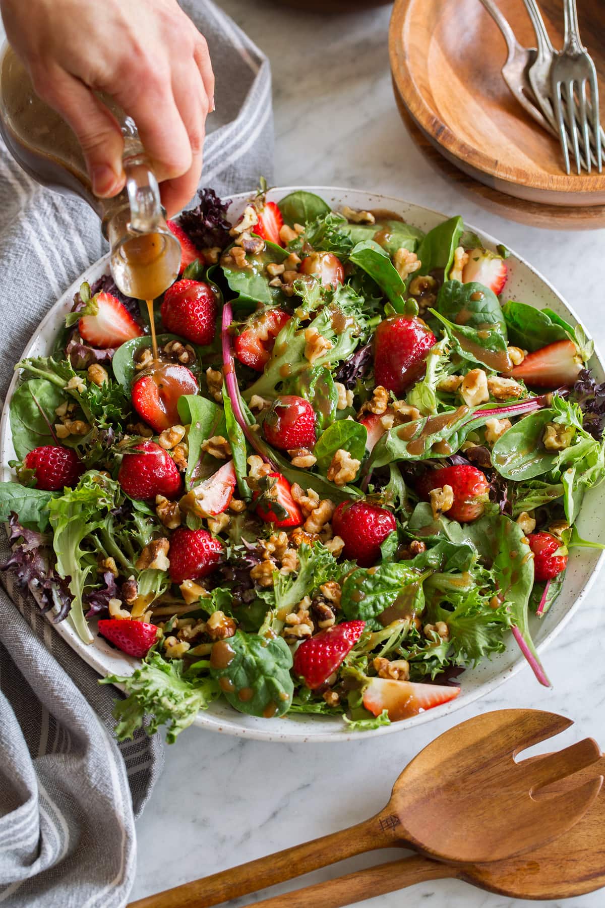 Green salad with strawberries and walnuts with balsamic vinaigrette being poured over.