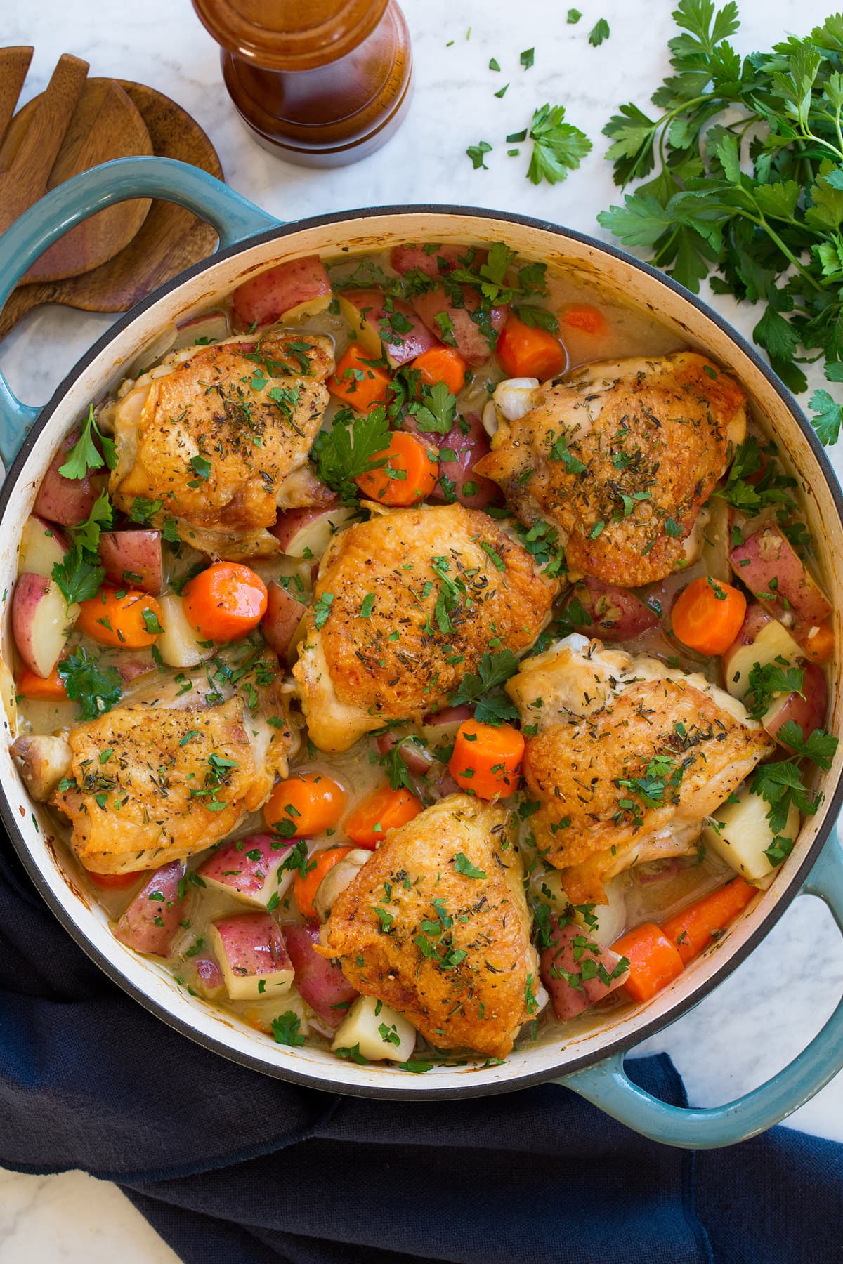 Braised chicken thighs with bones and skin in a braiser pot with carrots and potatoes.