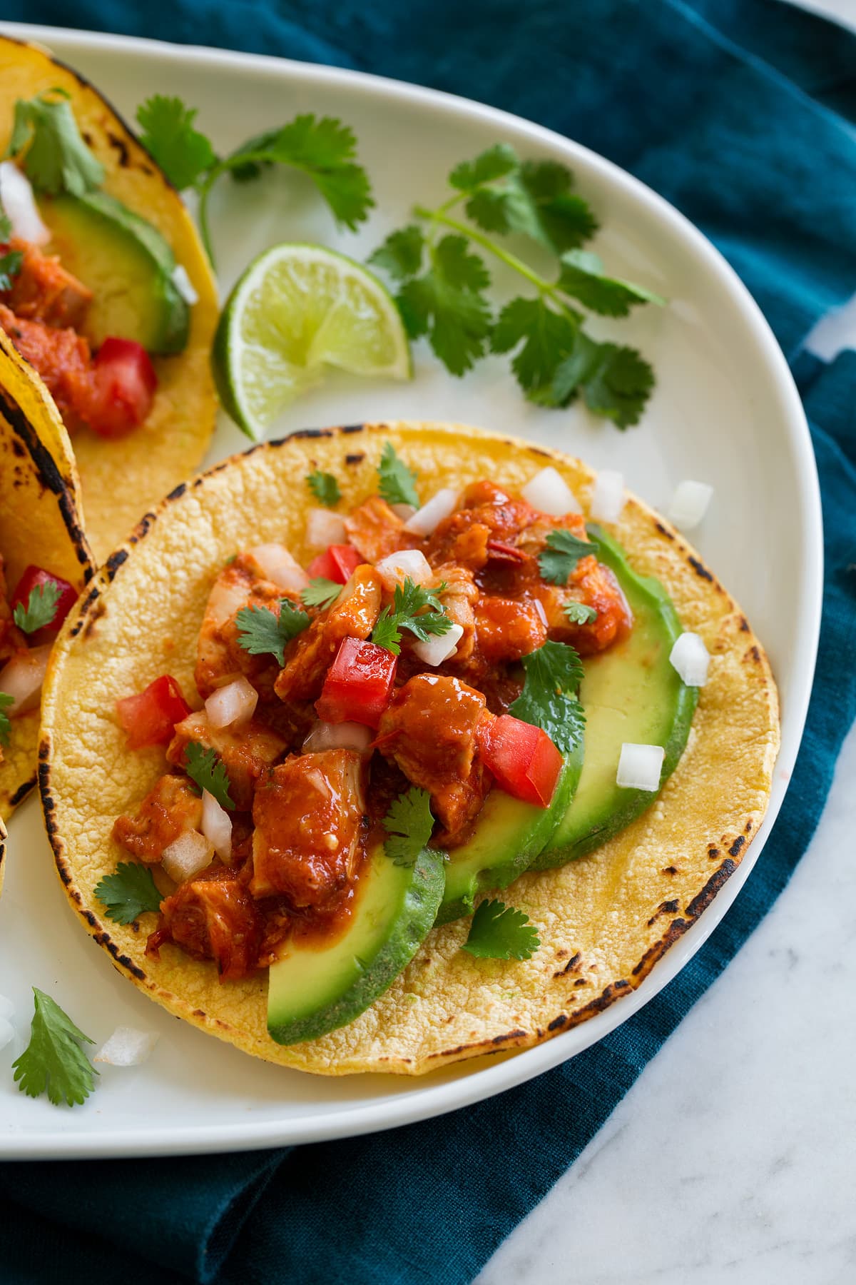 Chicken tinga served in a corn tortilla garnished with pico de gallo and avocado slices. 