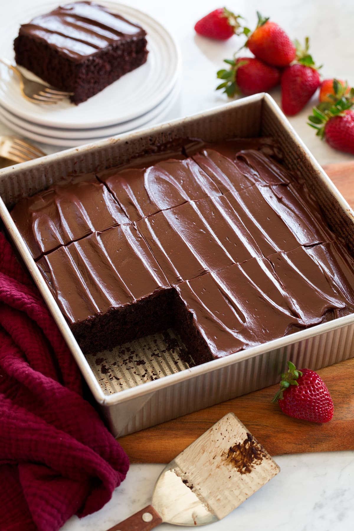 Sheet pan style chocolate cake shown in a metal 9 by 9-inch baking dish cut into squares and topped with optional icing.
