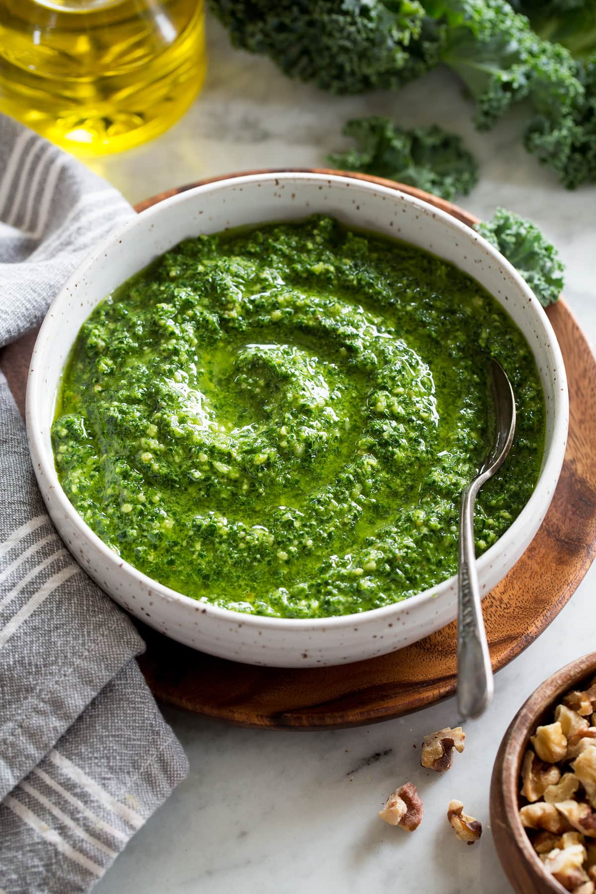 Kale pesto in a white bowl over a wooden plate. 