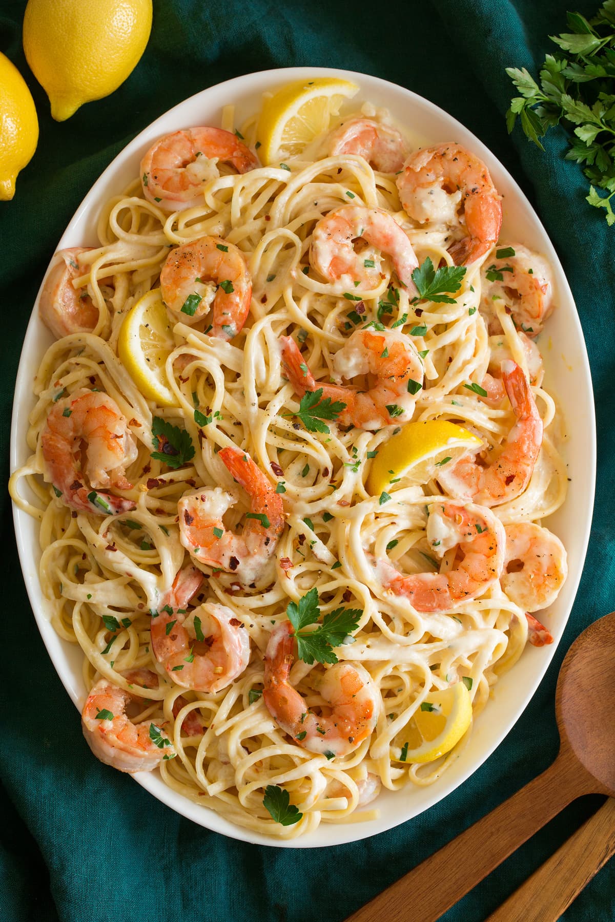 Shrimp pasta with creamy lemon sauce on a white oval serving platter shown from above. Platter is resting on an aqua colored cloth and lemons are shown to the side.