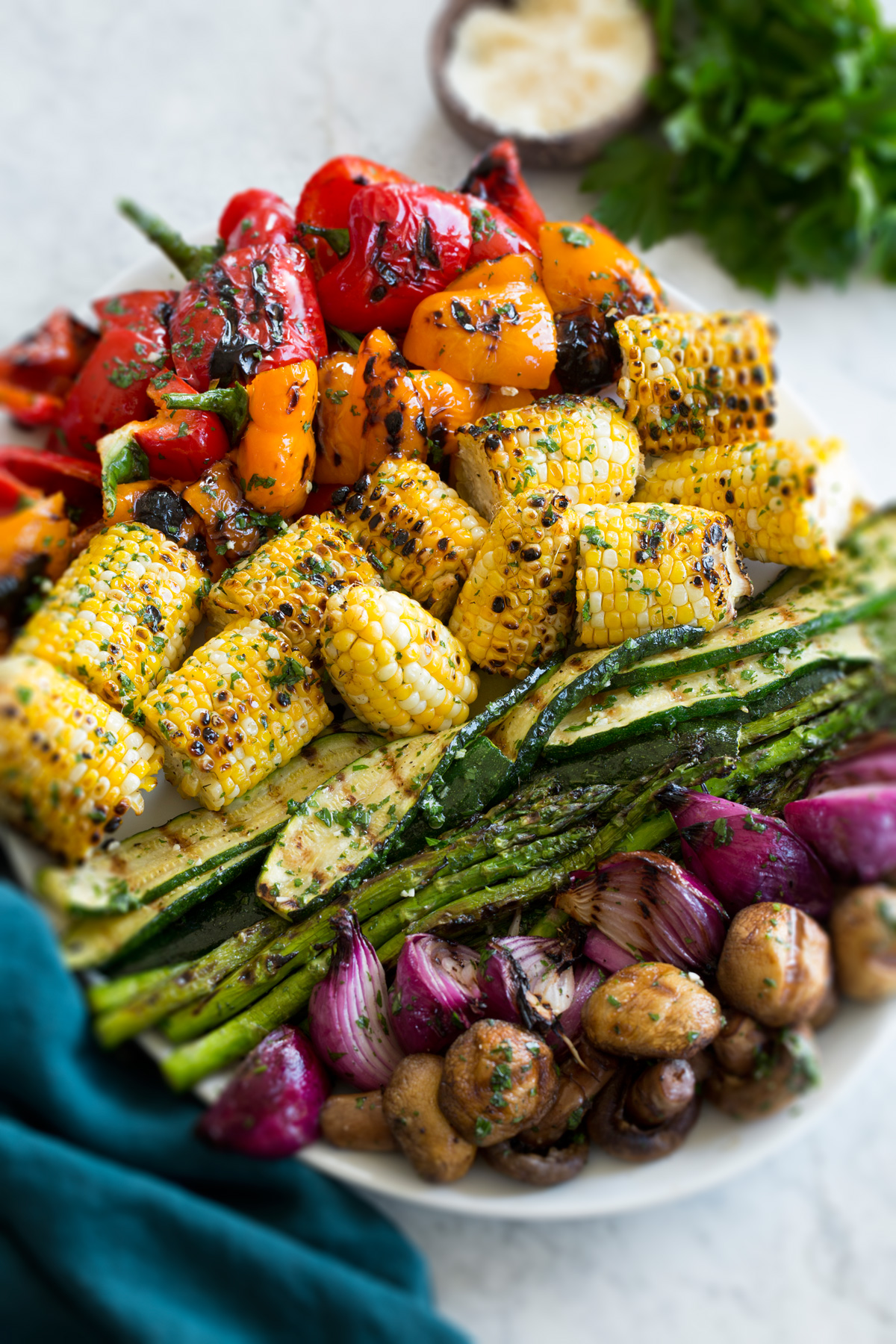 Grilled vegetables shown on an oval platter from a side angle with a blue cloth to the side.