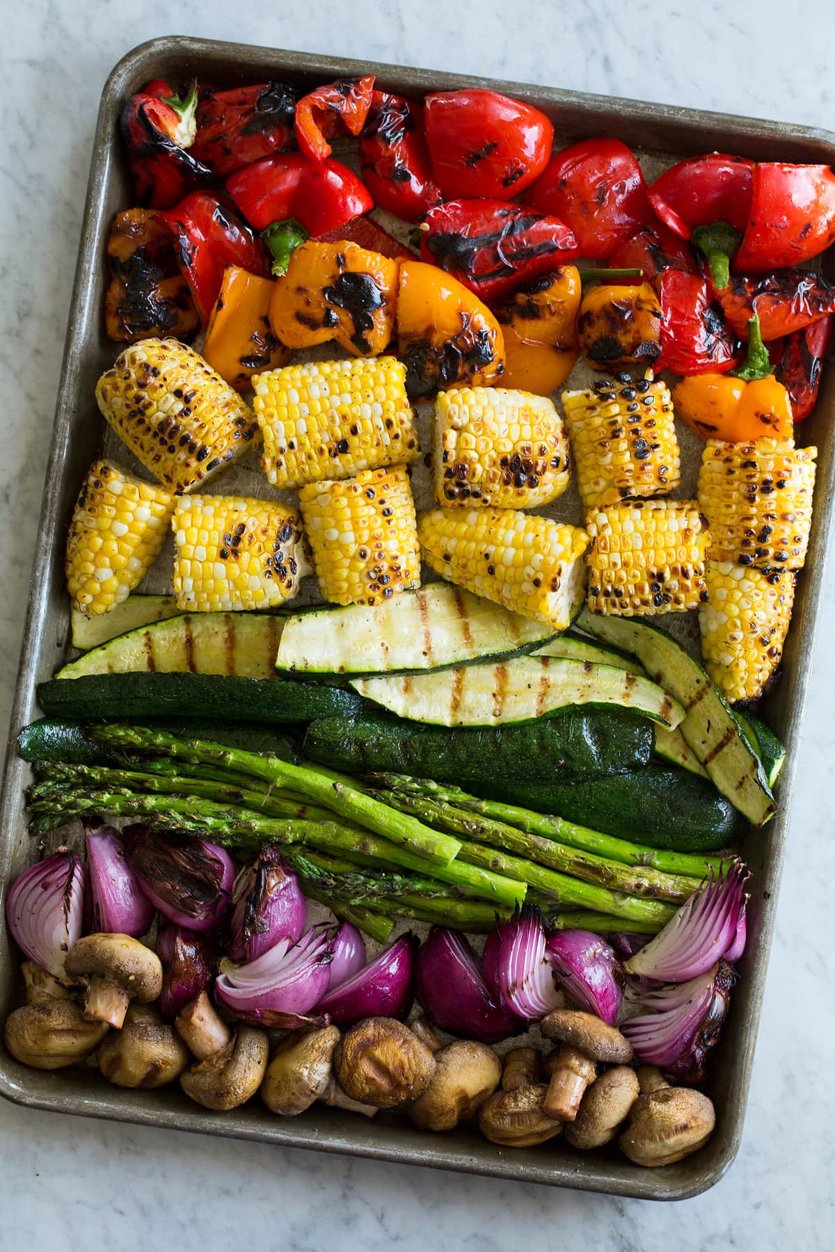Grilled vegetables on a baking sheet on a marble surface.