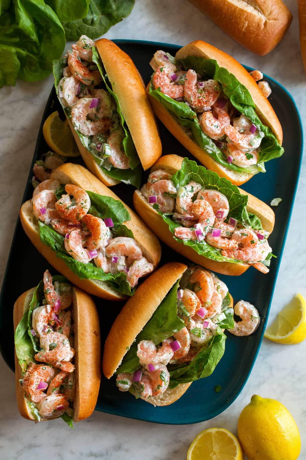 Shrimp Salad shown served in hoagie buns with lettuce leaves on a blue rectangular platter from above.