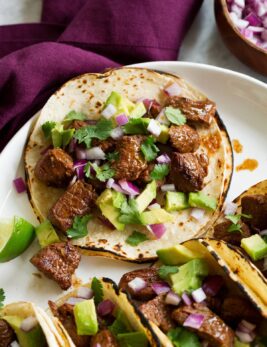 Single steak taco with avocado, cilantro and red onion shown close up.