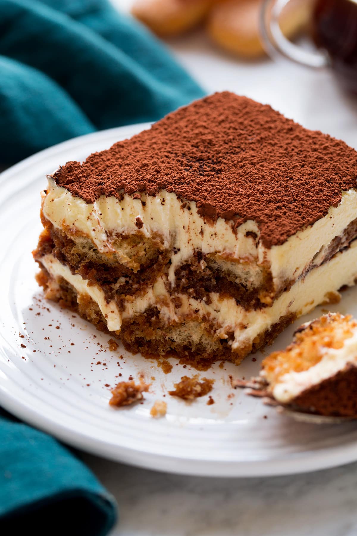 Close up photo of tiramisu cut into with a fork showing layers of custard filling, coffee soaked lady fingers and cocoa powder finish.