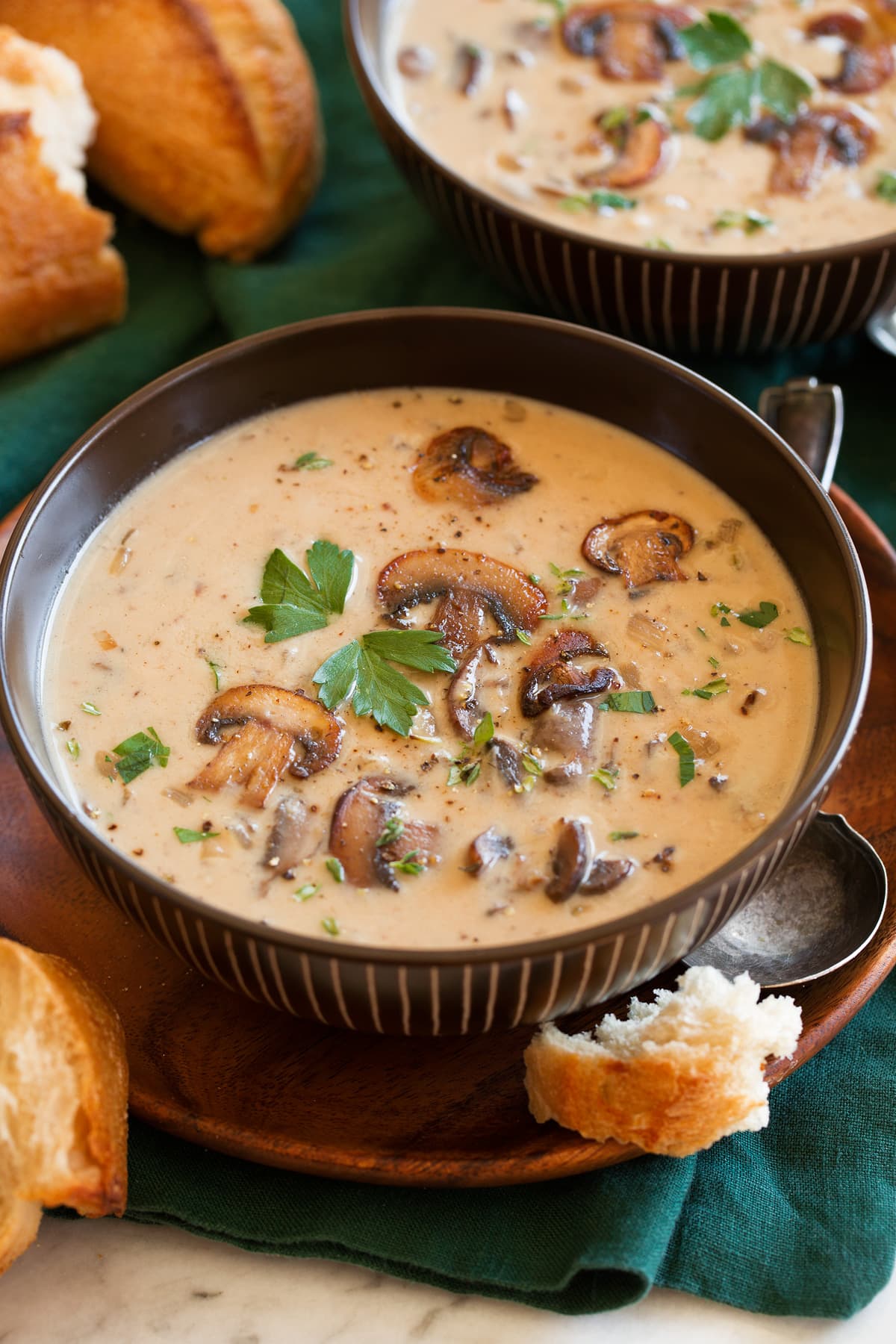 Single serving of cream of mushroom soup in a brown bowl garnished with sauteed mushrooms.