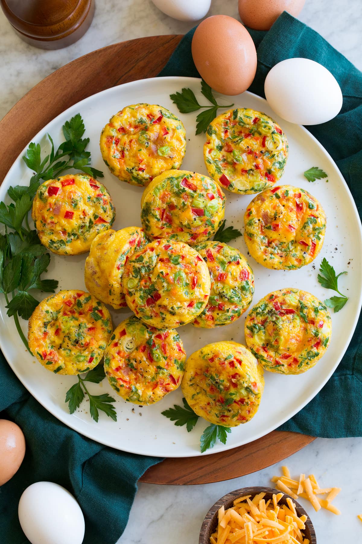 Egg muffins shown from above on a plate with eggs and cheddar cheese to the side.