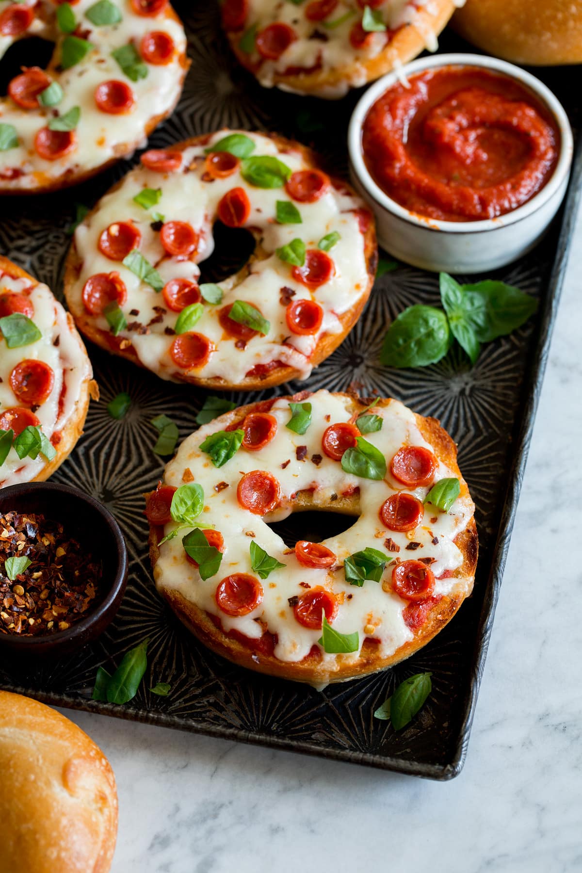 Pizza bagels shown close up with mozzarella cheese, pepperoni and basil over top.