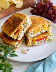 Two tuna melt sandwiches cut into halves and stacked on a large white plate.