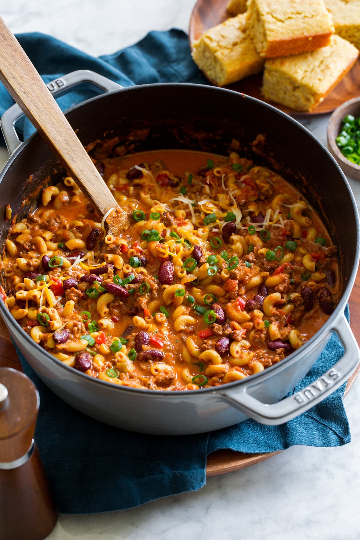 Chili mac in a large pot with a wooden spoon scooping mixture.
