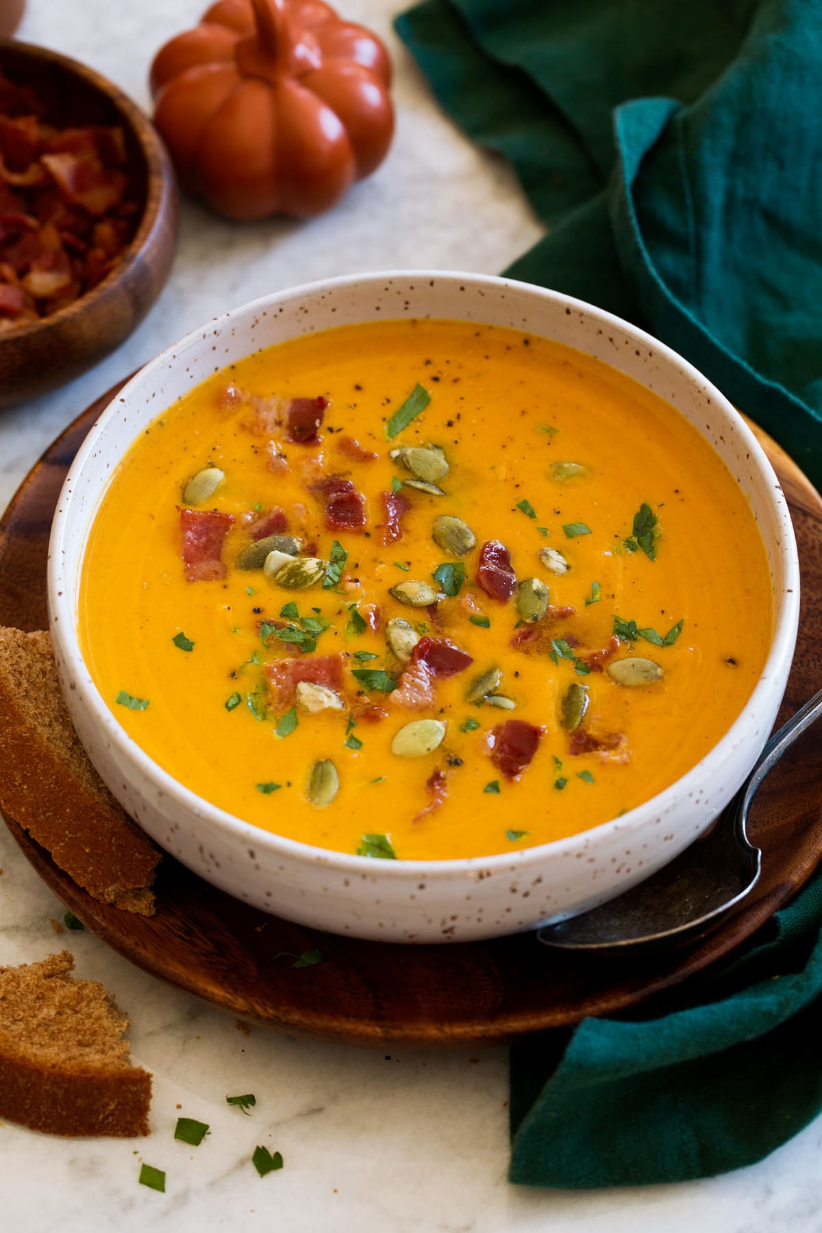 Monoporzione di zuppa di zucca condita con pancetta, prezzemolo e semi di zucca.