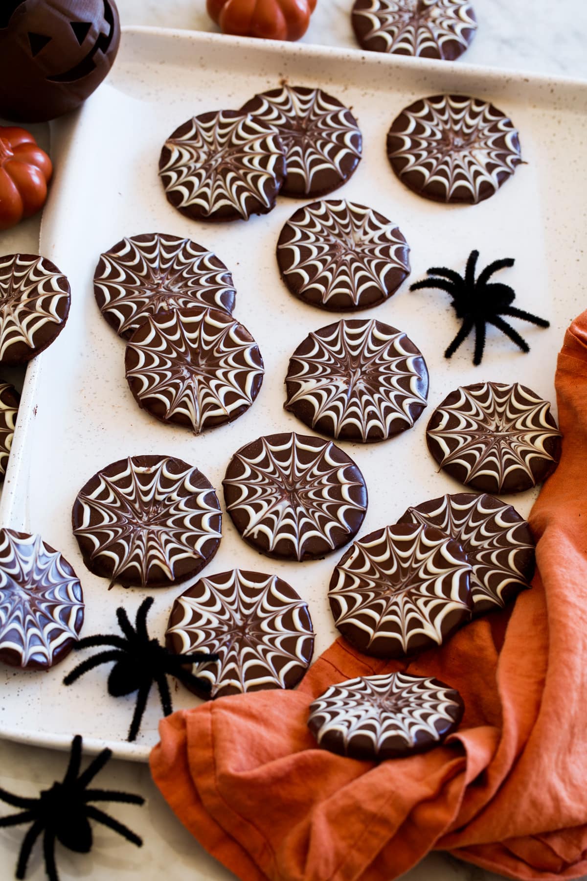 Spiderweb halloween cookies shown from the side on a white cookie sheet with decorate spiders to the side.