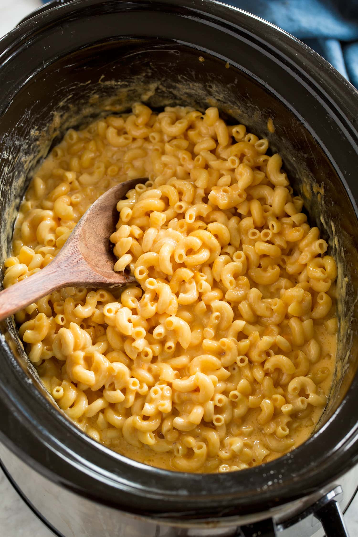 Crockpot Mac and Cheese in a slow cooker with a wooden spoon.