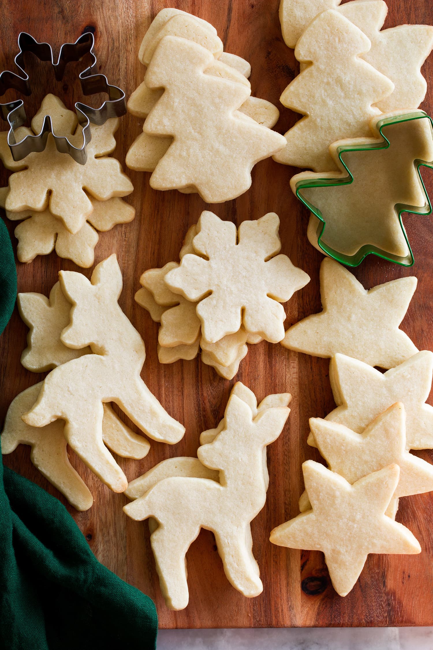 Baked cutout sugar cookies without icing shown on a wooden board with cookie cutters.