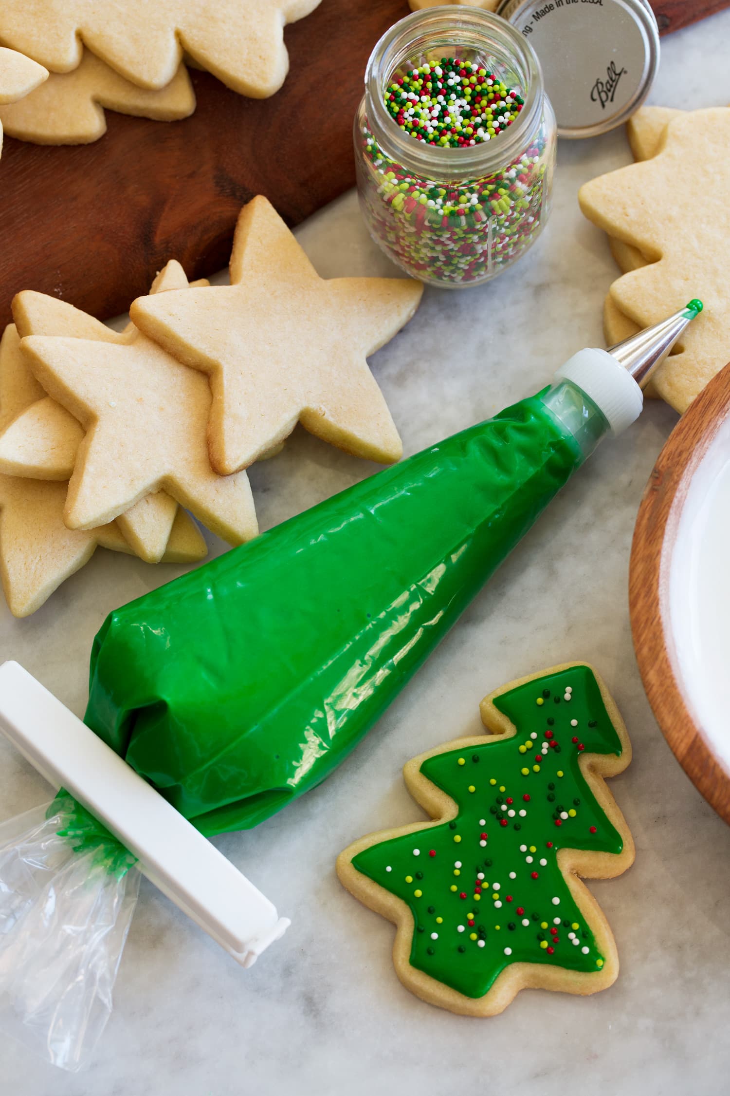 Glassa di biscotti di zucchero in una tasca da pasticcere.  La glassa è colorata di verde e accanto c'è un biscotto ritagliato che mostra come decorare con glassa e codette.