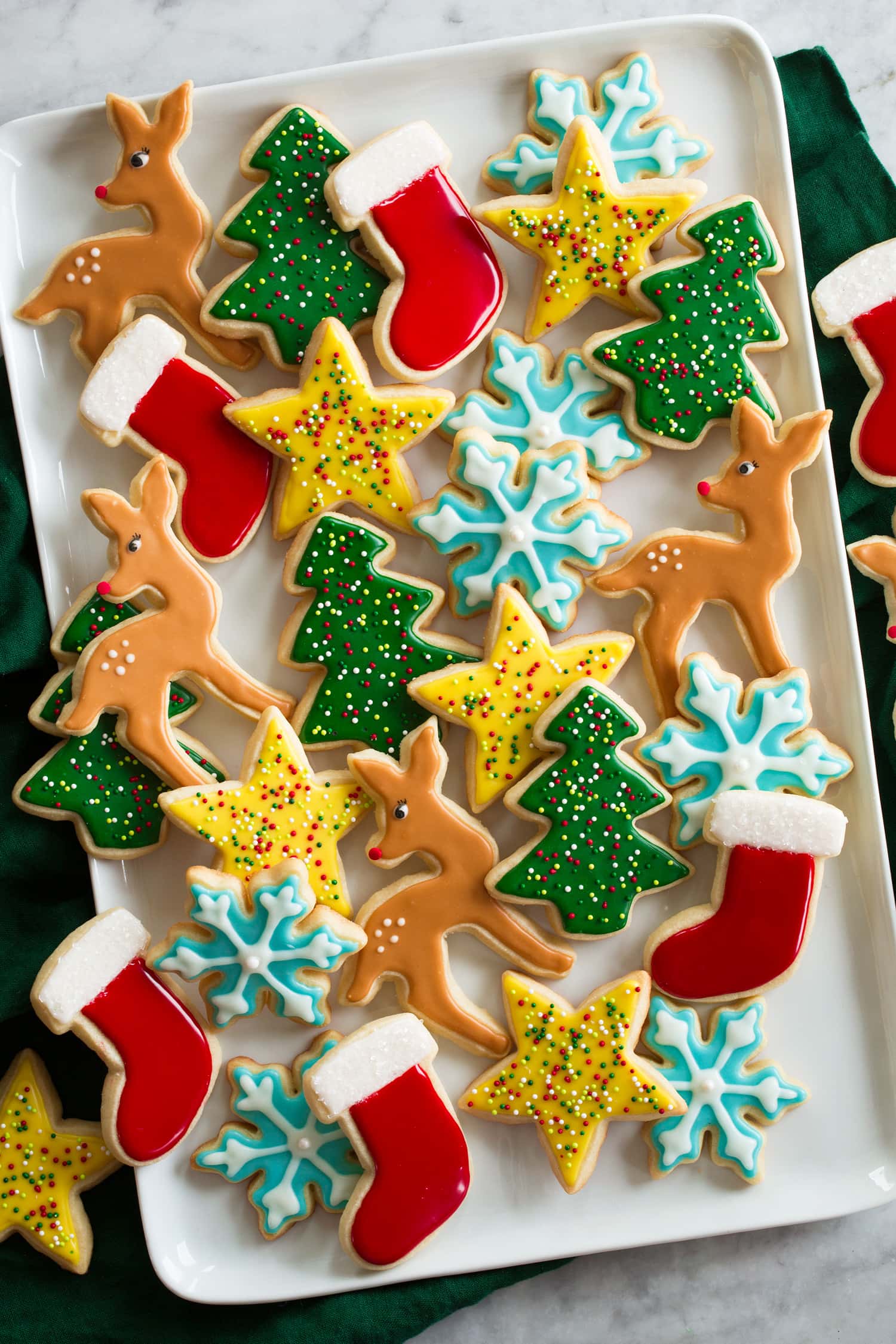 Cut out Christmas sugar cookies decorated with easy icing. Shown on a white rectangular platter from overhead. There are dear shapes, trees, stars, snowflakes and stockings.