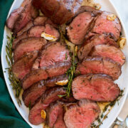 Beef Tenderloin arranged on a white oval platter shown from above on a white marble surface with a green cloth.