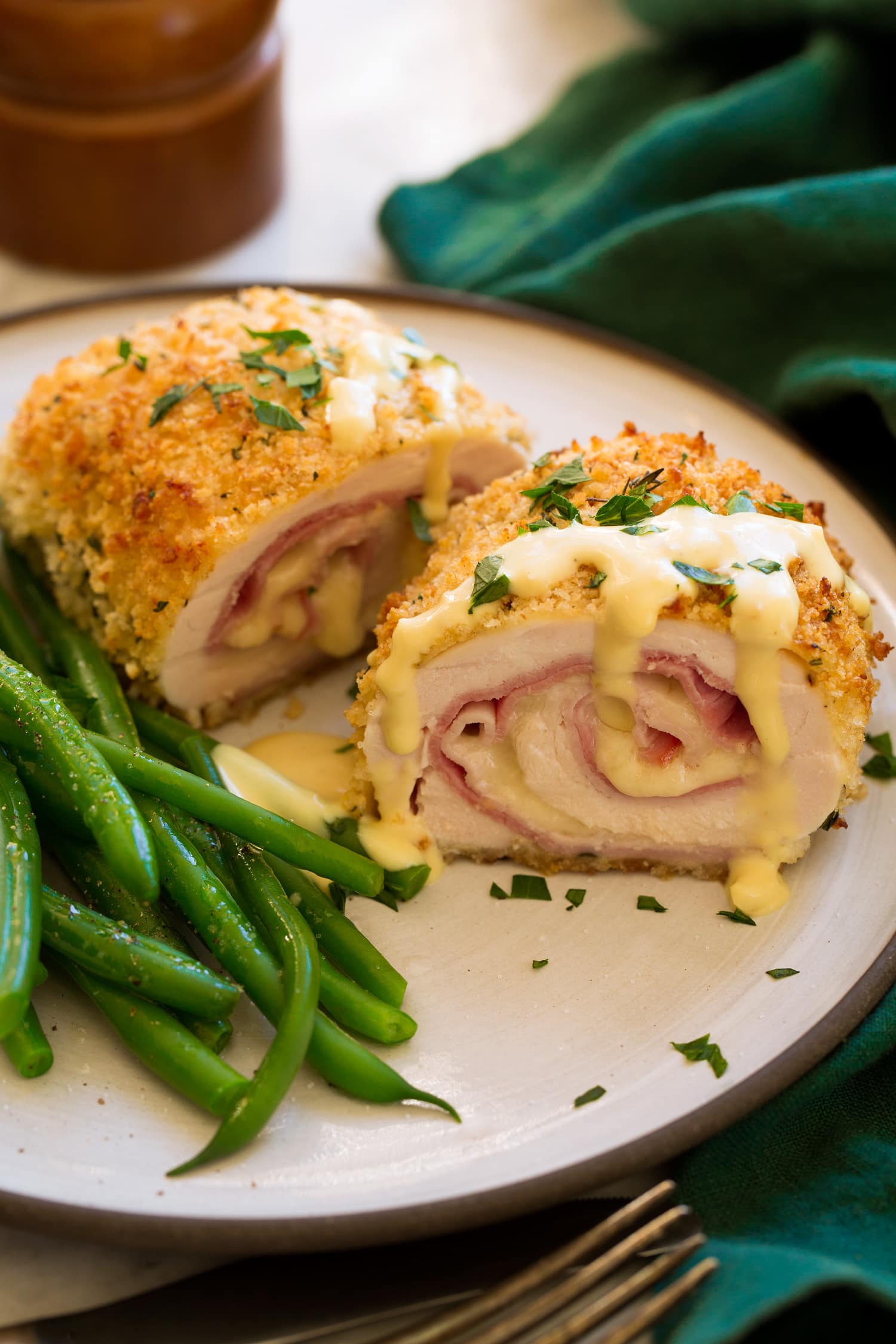 Chicken Cordon Bleu shown sliced in half with sauce on top. Green beans shown to the side.