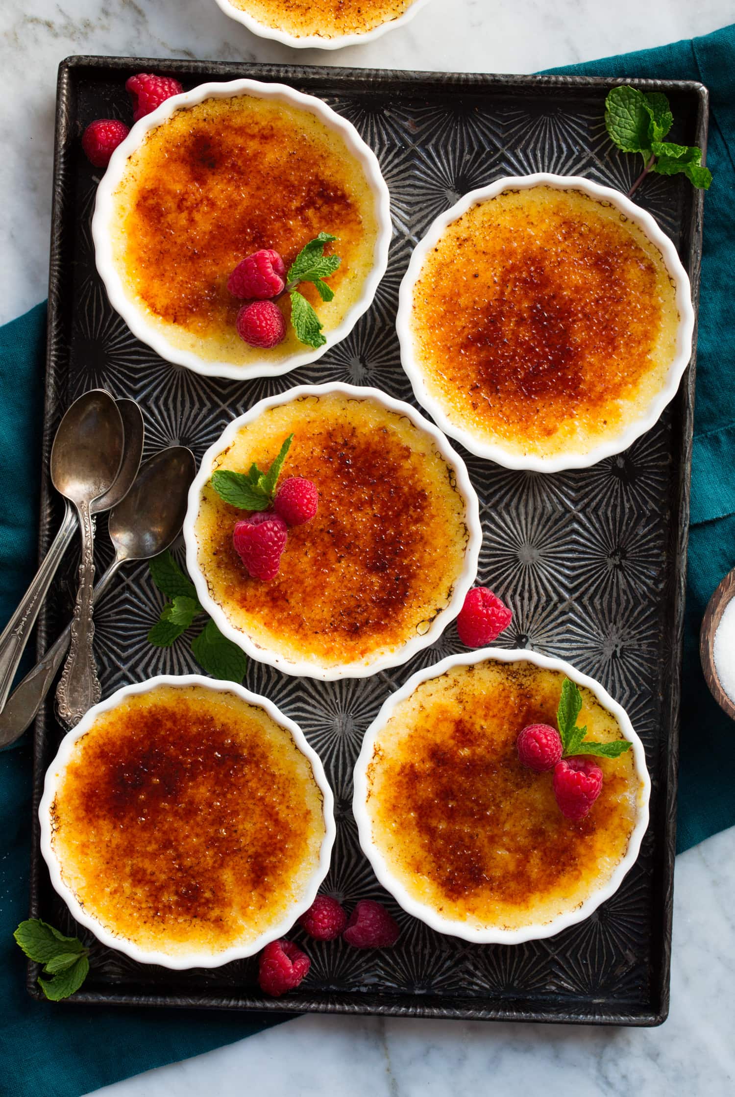 Overhead photo of five completed creme brûlée on a dark tray.