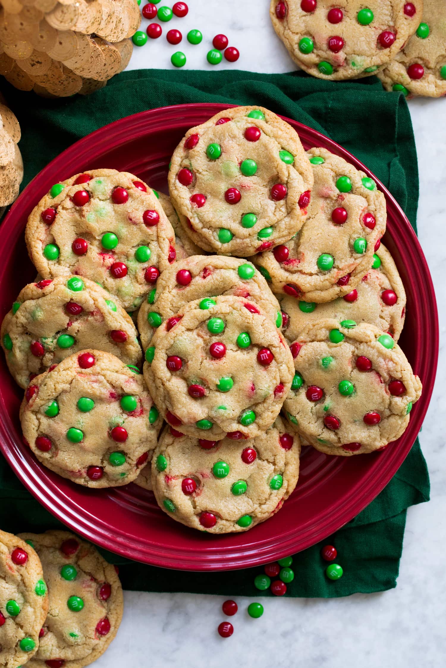 M and M Christmas cookies on a red plate over a green cloth.