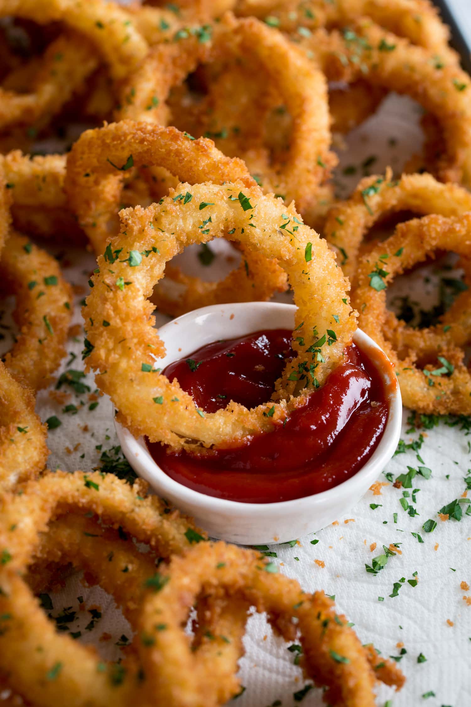 Homemade onion rings shown dipped in ketchup.