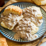Three buttermilk biscuits with sausage gravy on a blue plate.