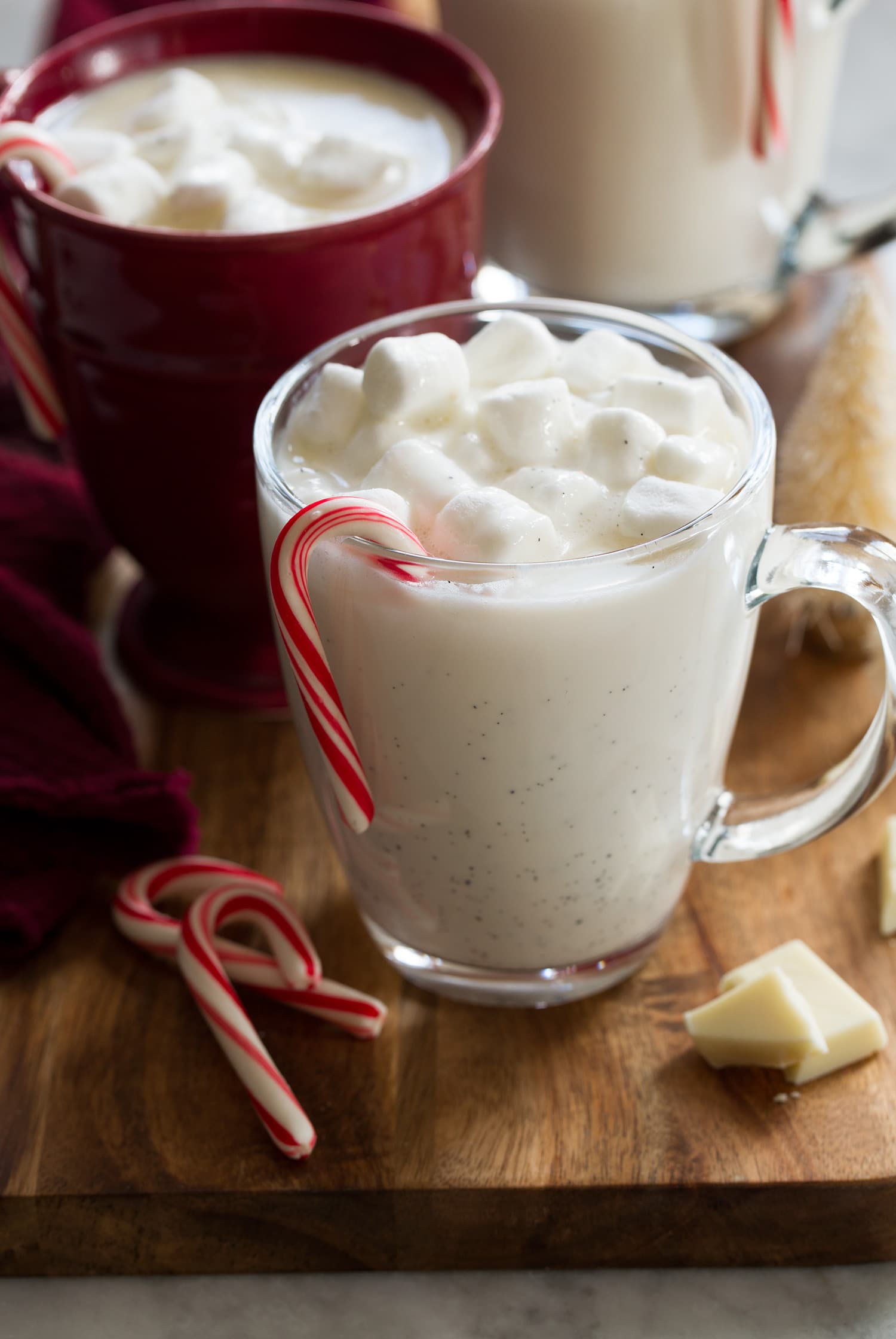 Close up photo of glass mug with white hot chocolate, marshmallows and candy cane. 