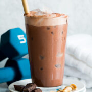 Homemade chocolate protein drink. Served on a stack of small plates with chocolate and peanuts to show flavor. Shown with weights in the back ground.