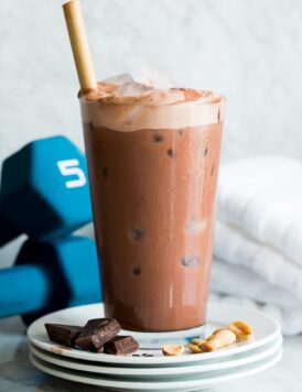 Homemade chocolate protein drink. Served on a stack of small plates with chocolate and peanuts to show flavor. Shown with weights in the back ground.