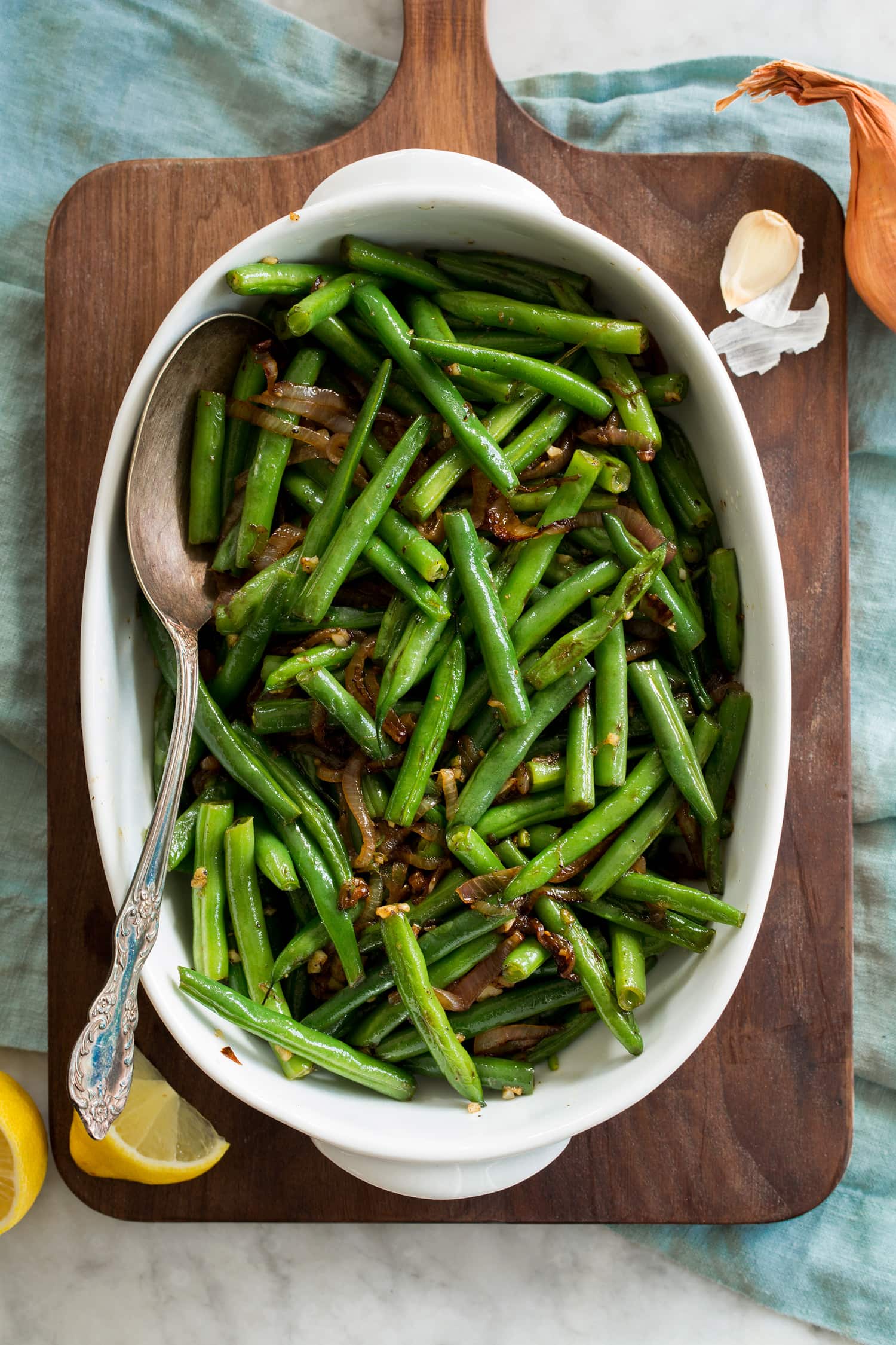 Sauteed green beans shown from above in an oval ceramic dish on a wooden tray.