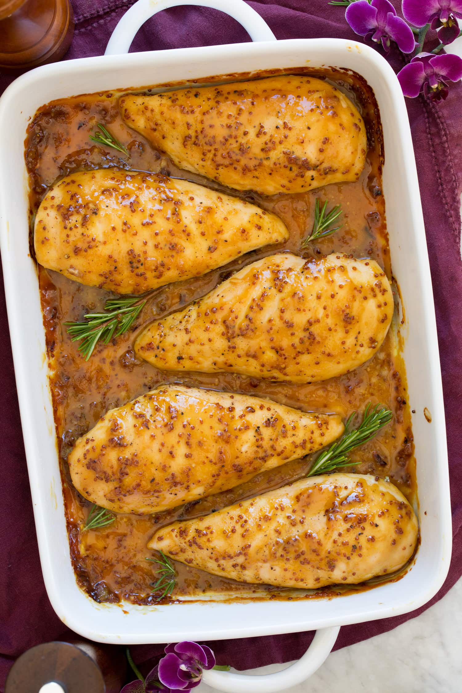 Whole grain mustard and honey chicken in white baking dish shown from above.