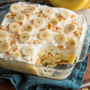 Banana pudding in glass square dish with scoop removed to show layers of the dessert.