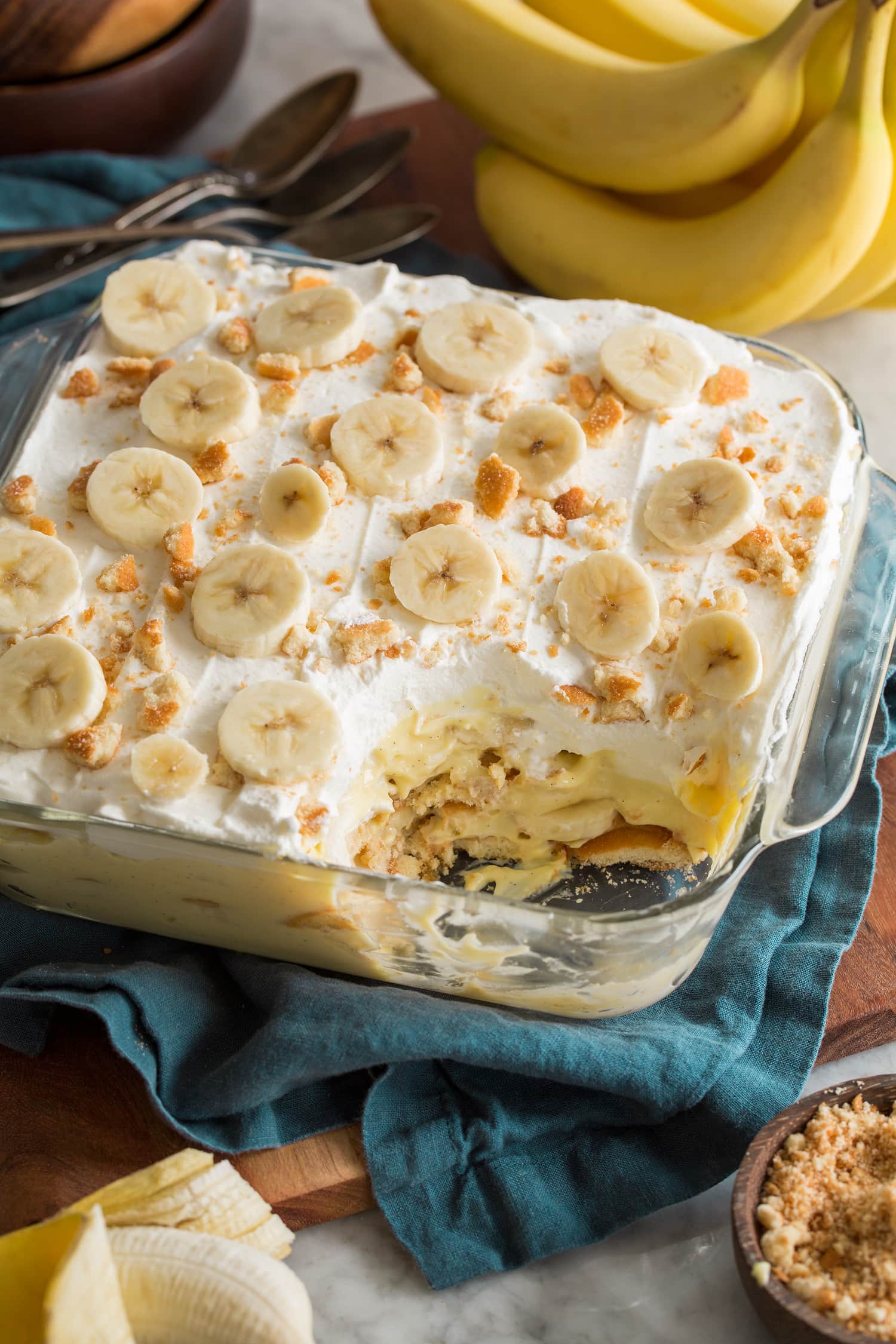 Banana pudding in glass square dish with scoop removed to show layers of the dessert.