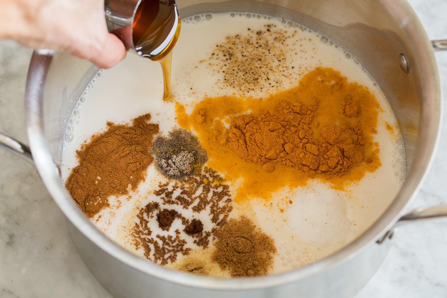 Showing how to make golden milk by mixing milk, spices and sweetener in pot.