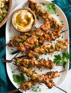 Shish tawook skewers on a platter with parsley and hummus.