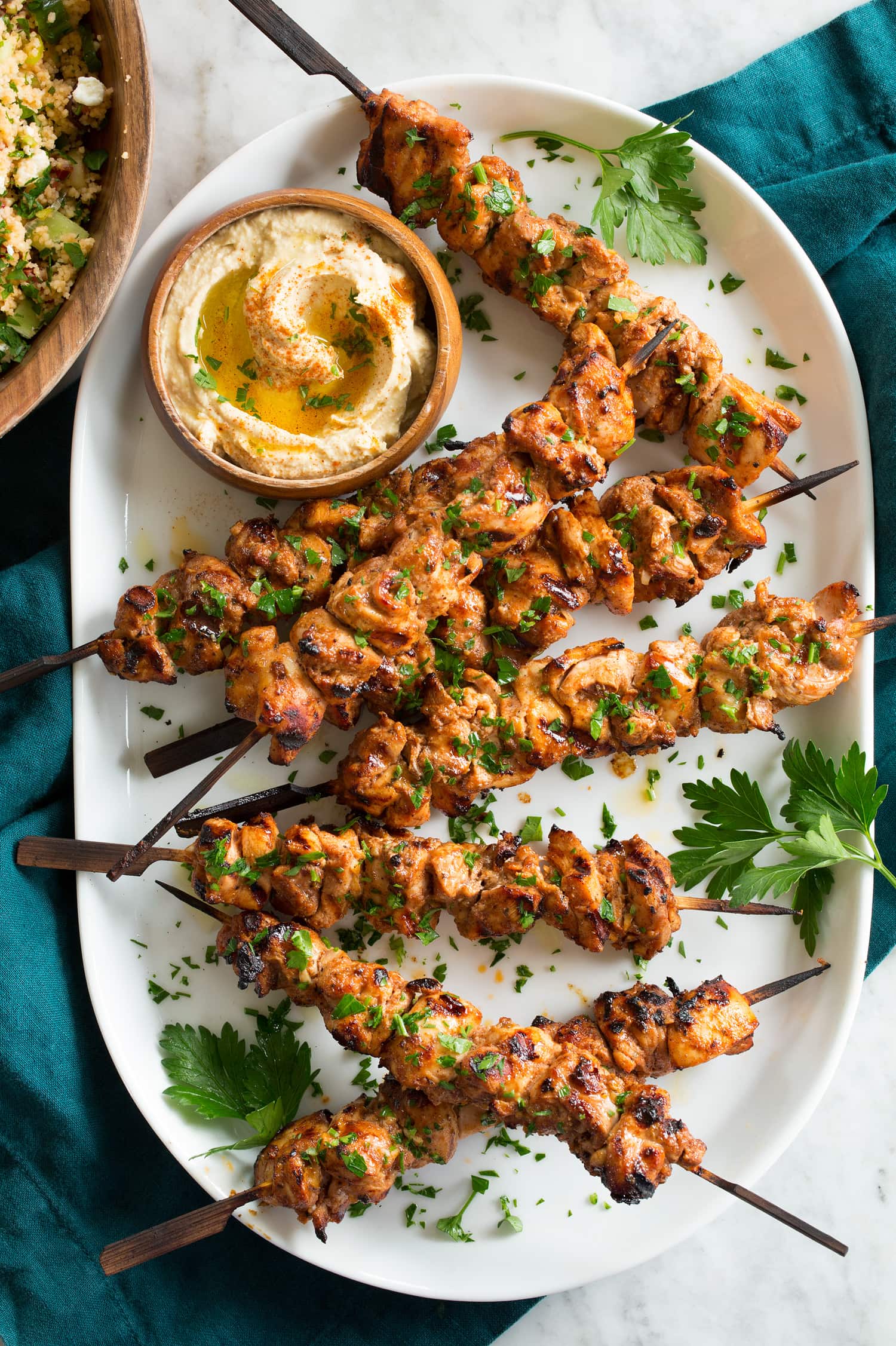 Grilled shish tawook skewers on a platter with parsley and hummus.