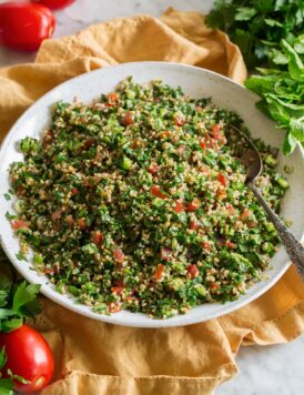 Herb tabbouleh shown in a white ceramic bowl over a yellow cloth.